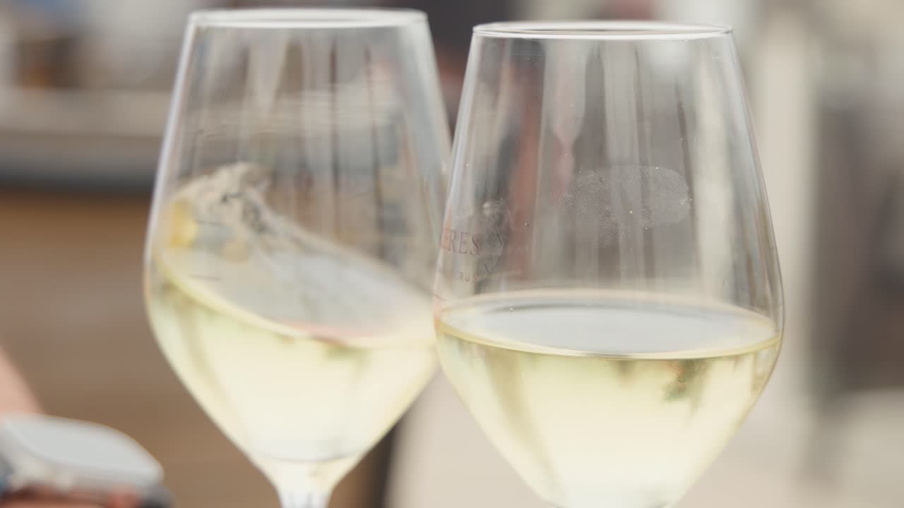 Due mani fanno risuonare calici di vino bianco sulla terrazza soleggiata di un bar con illuminazione naturale soffusa