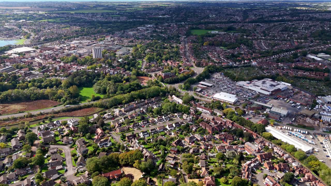 Aerial drone flies over Fareham town village in England, showcasing roads, fields, cars, and autumn trees glowing warmly in golden sunset light across the scenic countryside landscape