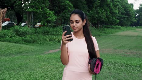 KOLKATA,INDIA:-Caucasian-sporty-girl-young-adult-in-her-20-s-with-yoga-mat-isolated-on-outdoor-background-using-cell-phone