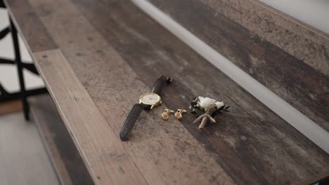brown leather watch, gold cufflinks, and white boutonniere arranged on rustic wood surface