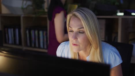 Video-of-focused-caucasian-woman-using-computer,-working-late-in-office