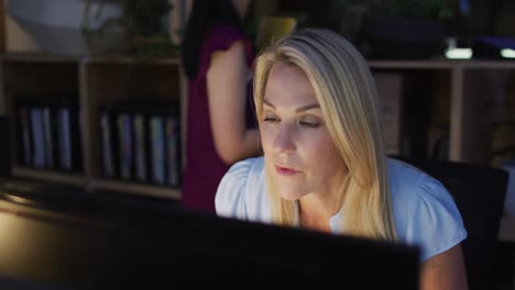 video de una mujer caucásica enfocada usando una computadora, trabajando hasta tarde en la oficina