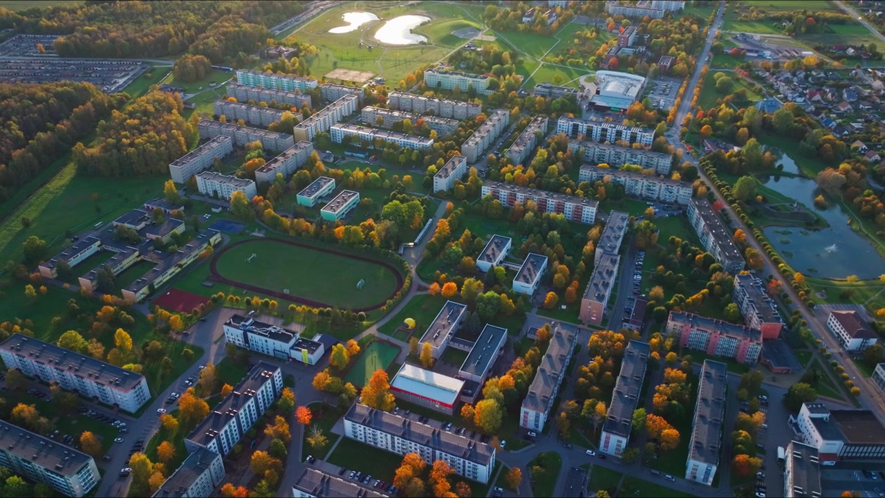 Cinematic orbit drone shot above Naujoji Akmene glowing in autumn sunset light