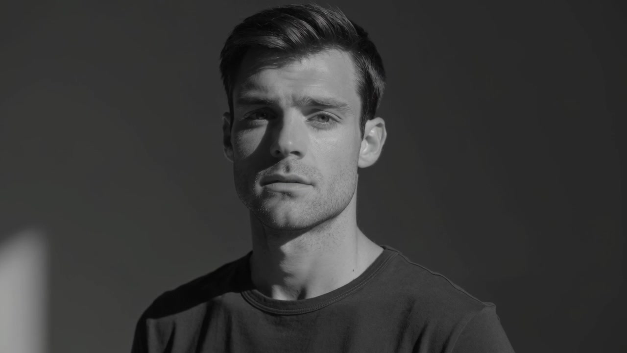 Filming male model in dark top shifting facial expression at backdrop for portrait, with side light