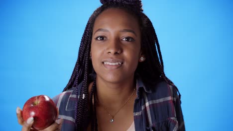 close-up of a young african-american woman taking a bite of an apple against a blue background.