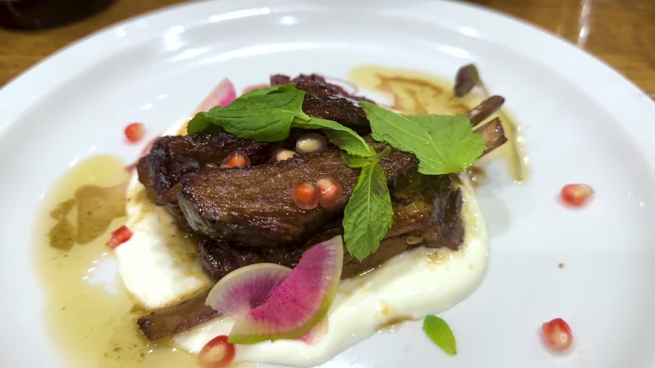 A beautifully plated rib steak with fresh greens, pomegranate seeds, and vibrant garnishes on a white plate