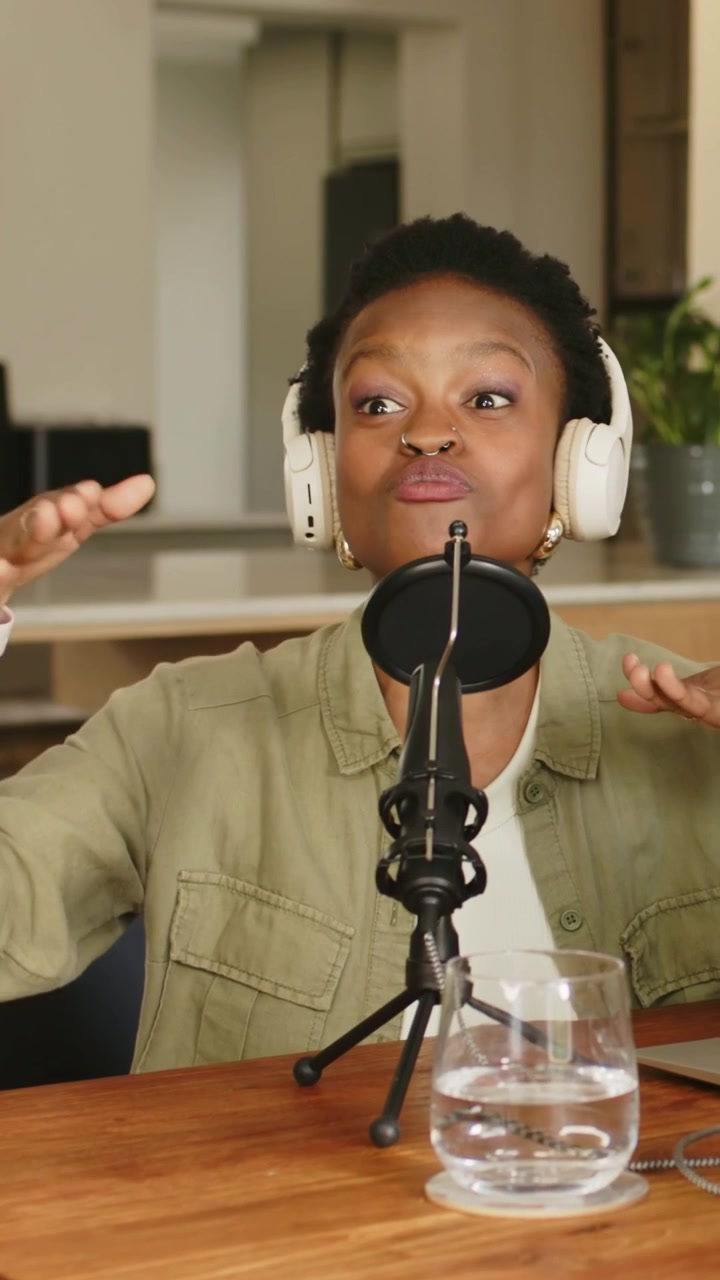 Vertical video: Smiling at cue host wearing headset olive top podcasting into mic at home table