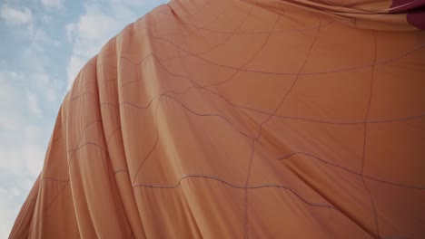 orange color hot air balloon deflating on ground against blue sky, handheld view