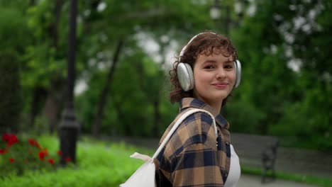 happy brunette girl wearing headphones posing while walking in the park. finishing classes at the university and taking a walk in the fresh air