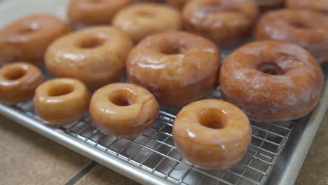 homemade glazed donuts on cooling rack with mini and full size, handheld detail