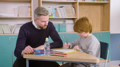 redheaded student sitting at the desk in english classroom while the teacher answers him some questions