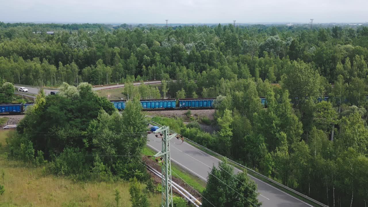 Cars wait at railroad crossing as freight Train hauls coal trucks AERIAL