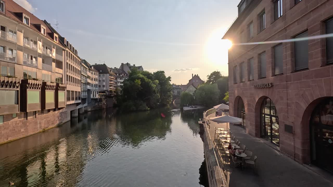 Camera smoothly pans along historic riverside buildings at sunset in Nuremberg, Germany, revealing calm water, outdoor seating, and warm natural lighting