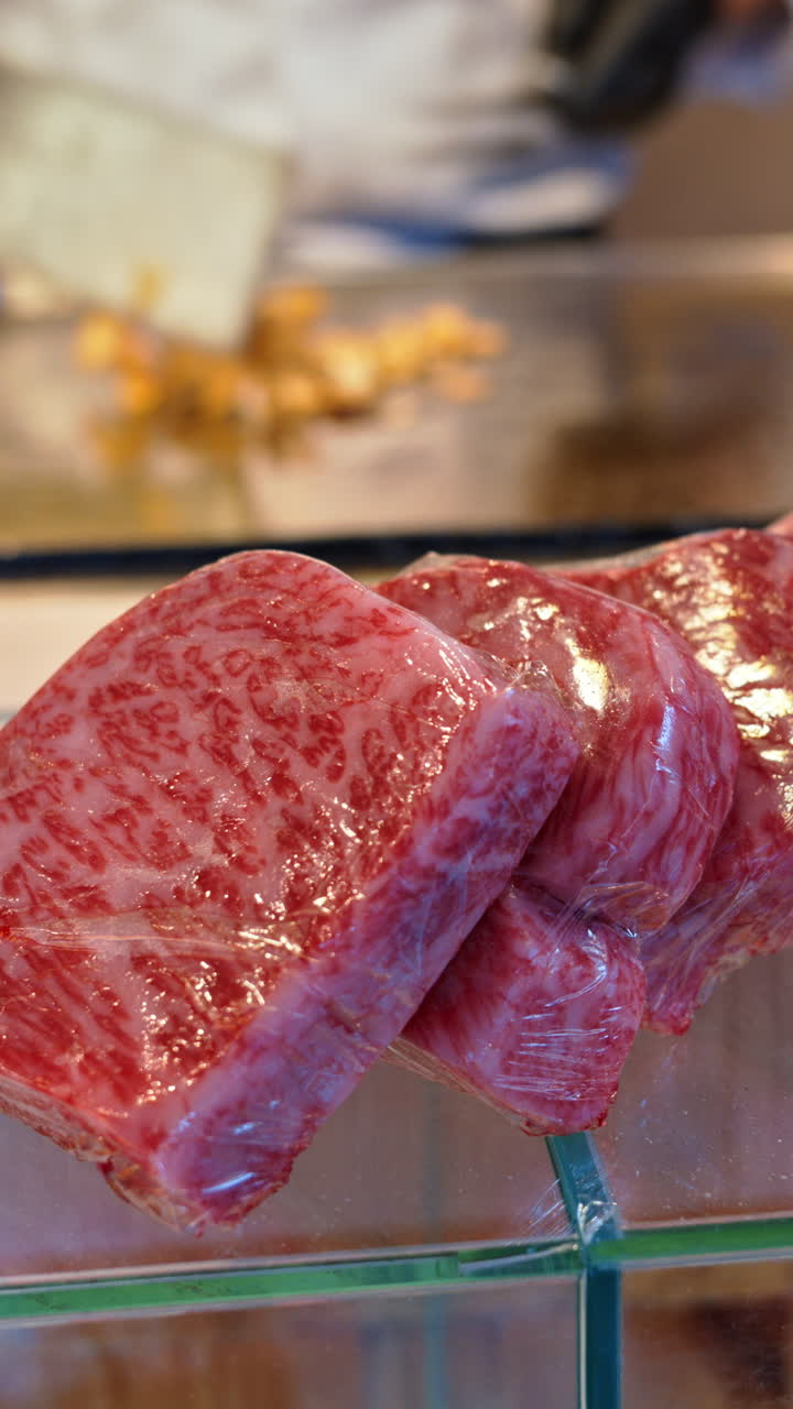 Close up of multiple pieces of Wagyu beef with a chef cooking in the background at the Tsukiji Fish Market in Japan. Vertical