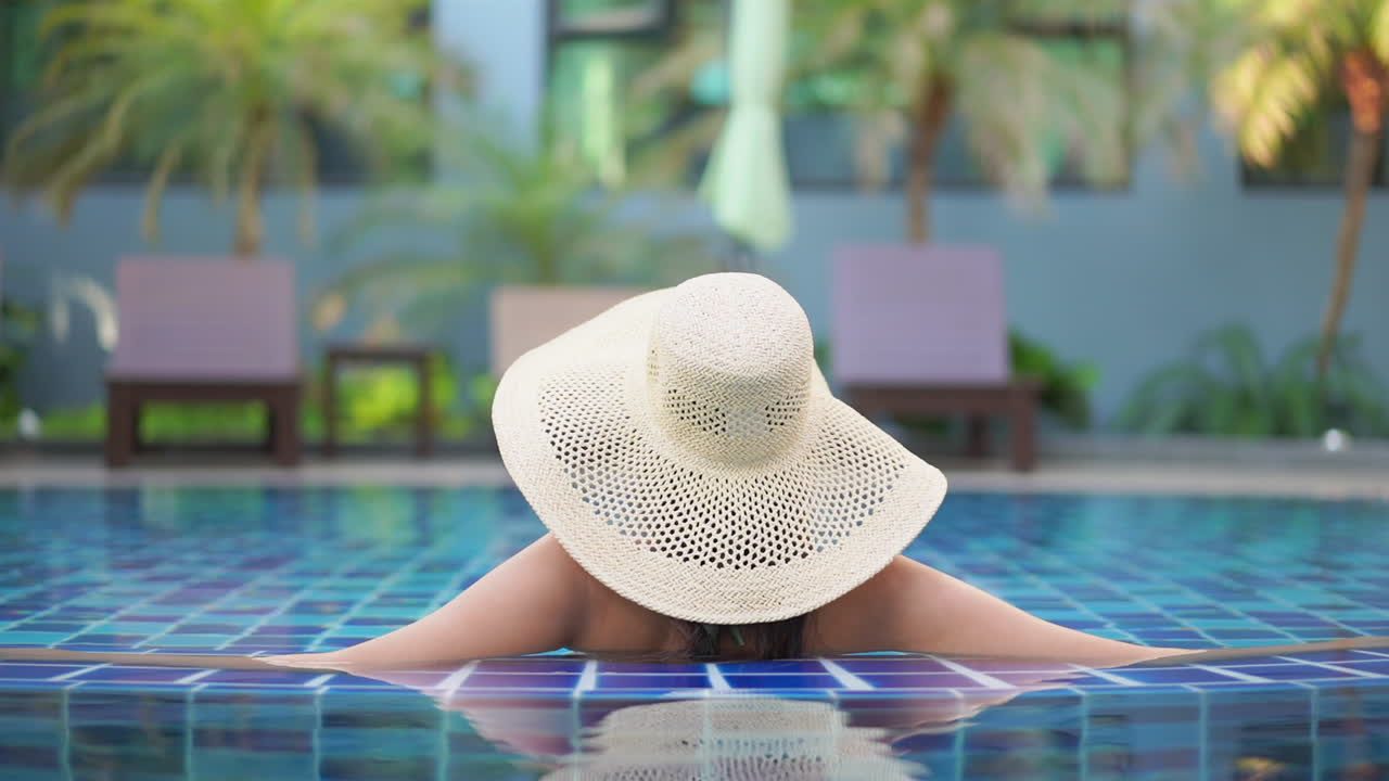 Eine junge Frau mit einem schlaffen Sonnenhut aus Stroh lehnt sich an den Rand eines Infinity-Pools