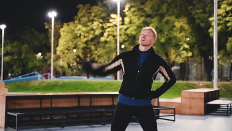 sportive blond man doing stretching exercises before training in the park at night