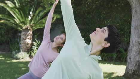 Feliz-Pareja-De-Lesbianas-Caucásicas-Practicando-Yoga-En-Un-Jardín-Soleado,-Cámara-Lenta