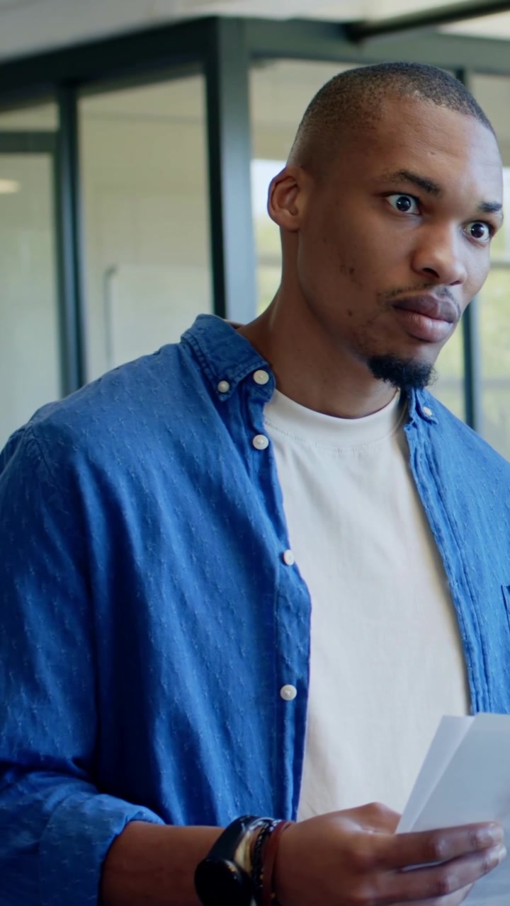 Vertical video: Holding docs after colleague speaks, man in denim shirt scanning them at office