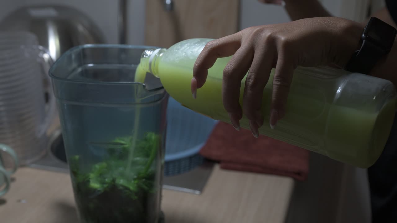 Young woman preparing fresh green organic smoothie at home kitchen made from kale and guava juice