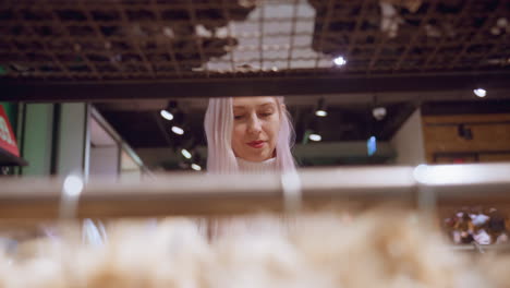 rack view mall goer smiling fixing eyes on cloth she holds and inspects under bright boutique lighting amid organized winter apparel racks evoking relaxed shopping experience and tactile discovery
