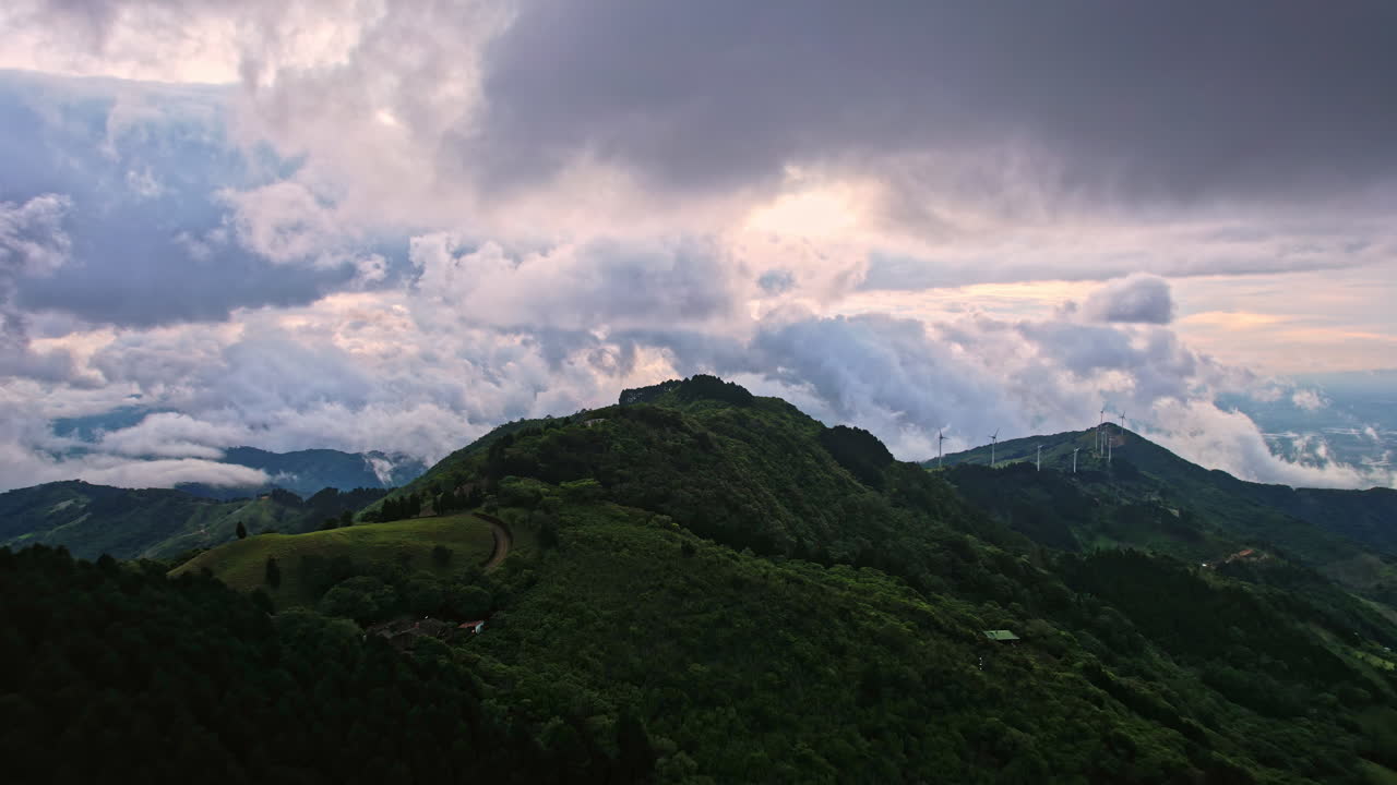 웅장한 풍력 터빈은 녹색 언덕과 극적인 산 사이에서 높이 서 있습니다.
