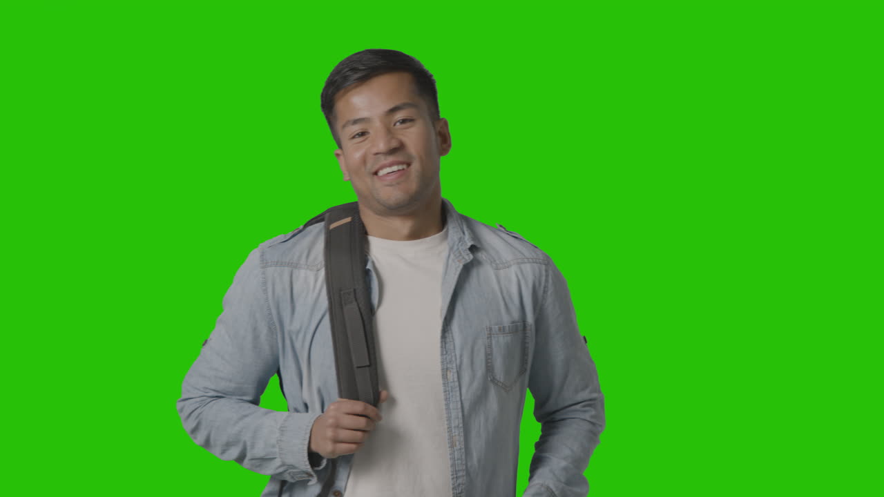 retrato de un estudiante universitario o universitario masculino sonriente poniéndose una mochila lista para la clase contra la pantalla verde