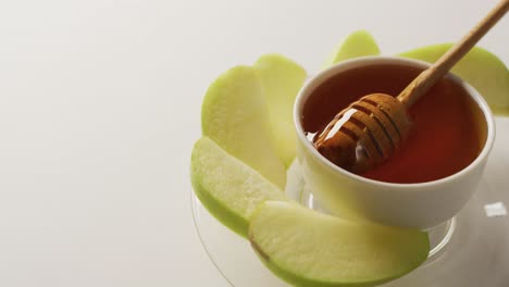 Video-of-honey-in-jar-and-apple-slices-lying-on-white-surface