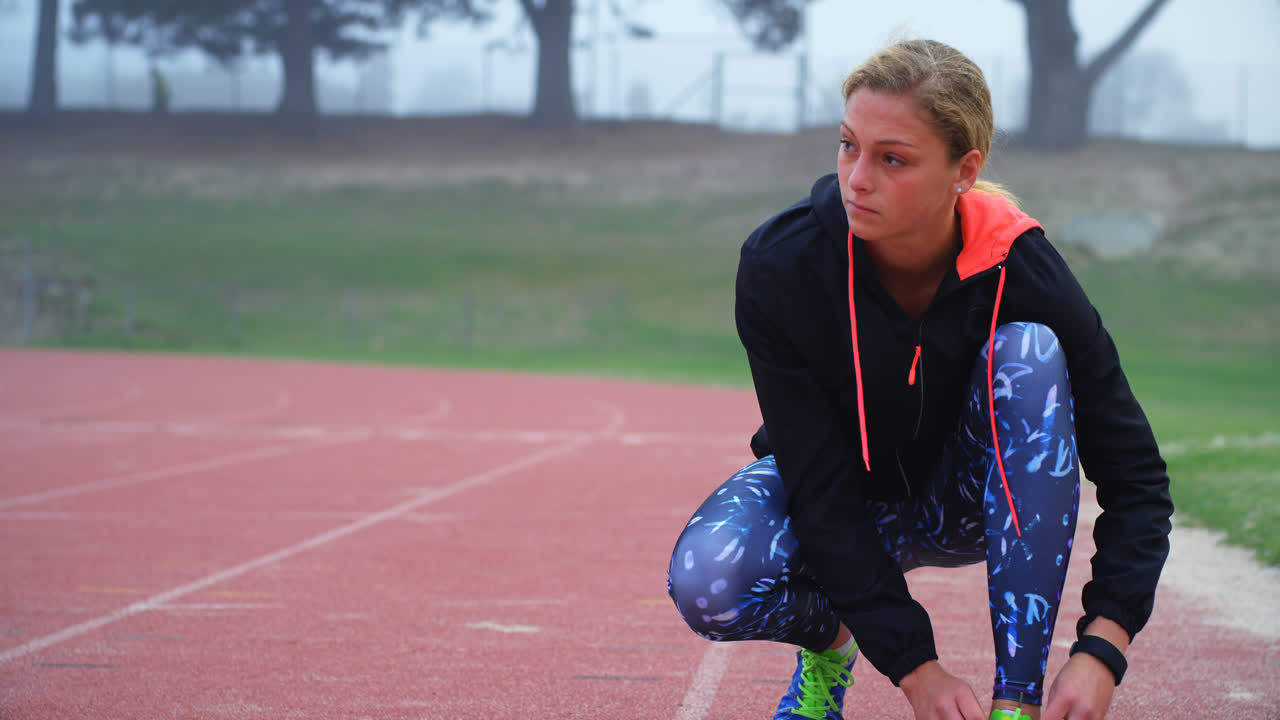스포츠 장소에서 달리기 트랙에서 신발을 는 젊은 백인 여성 운동 선수의 전면 뷰 4k