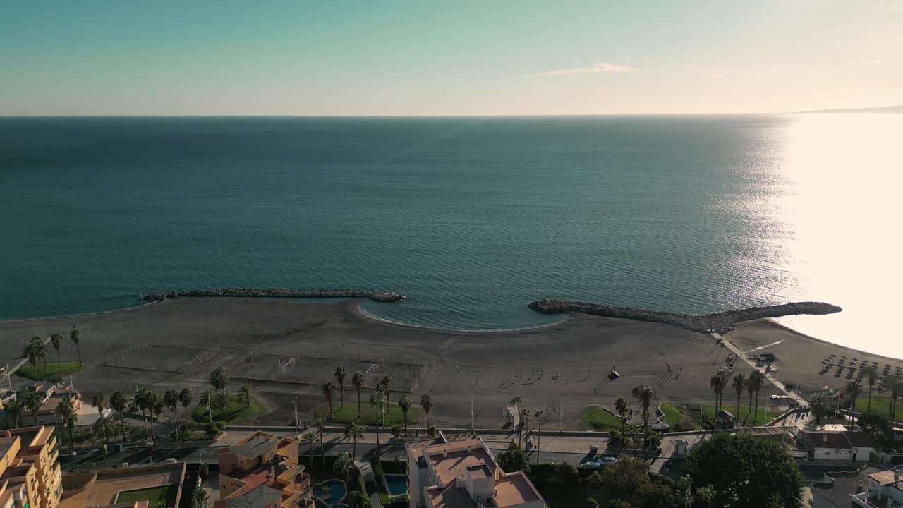 Spiaggia vuota di Malaga all'alba con acque calme e orizzonte sereno.