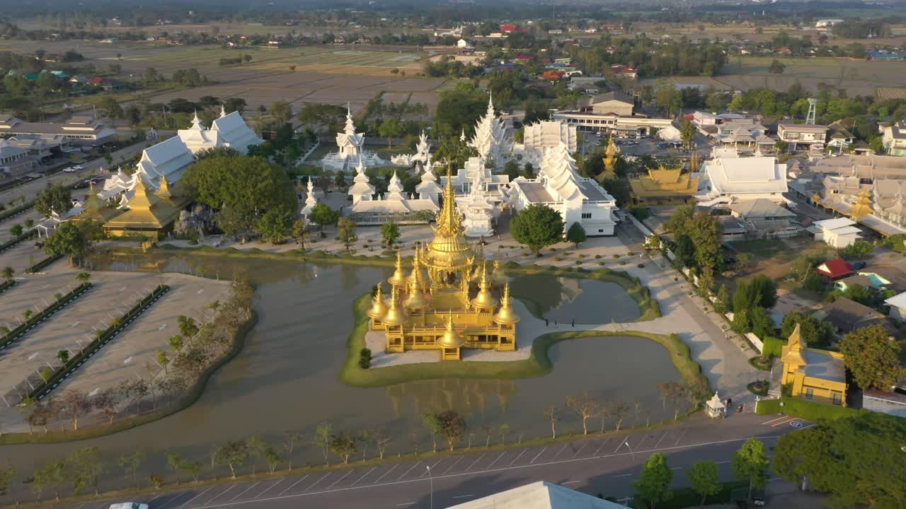 drone aéreo volando hacia atrás de wat rong khun el templo budista gigante blanco y el templo dorado con montañas y paisaje en chiang rai, tailandia