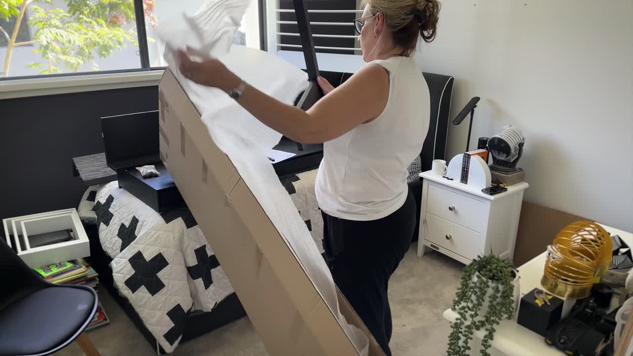 A mature woman unwrapping flat-pack furniture from a box in a kid's bedroom