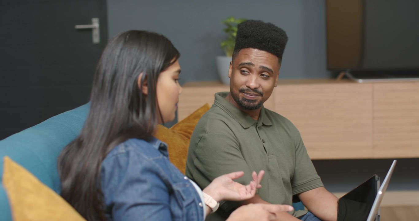 African team on blue sofa, woman starting talk gesturing clarifying task while man using laptop