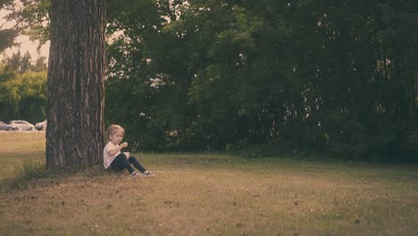 young-lady-takes-object-from-mouth-sitting-at-tree-trunk