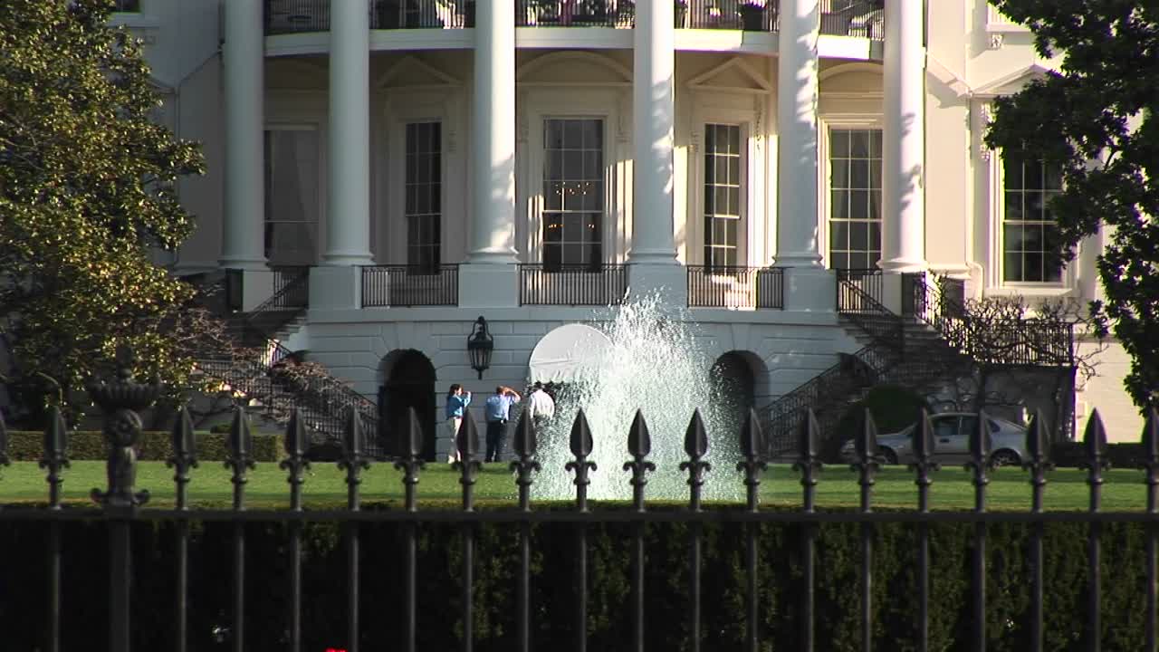 카메라는 백악관 2층 발코니를 걷고 있는 여러 사람을 보여주기 위해 위로 움직입니다.