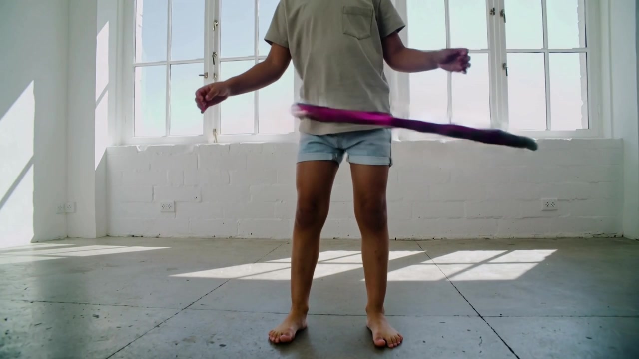 Hooping child starting to keep hula-hoop rotating by loft windows, in light tee and denim shorts