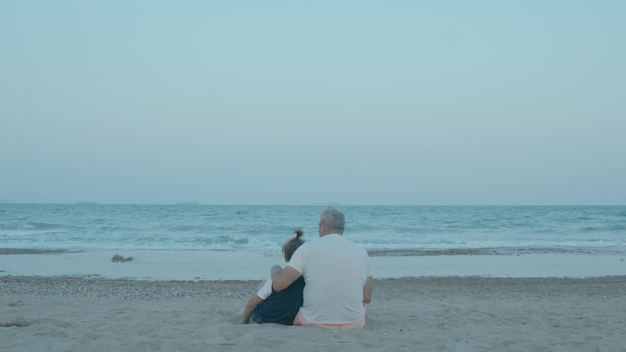 한 남자 와 한 소년 이 해변 에 앉아 있다