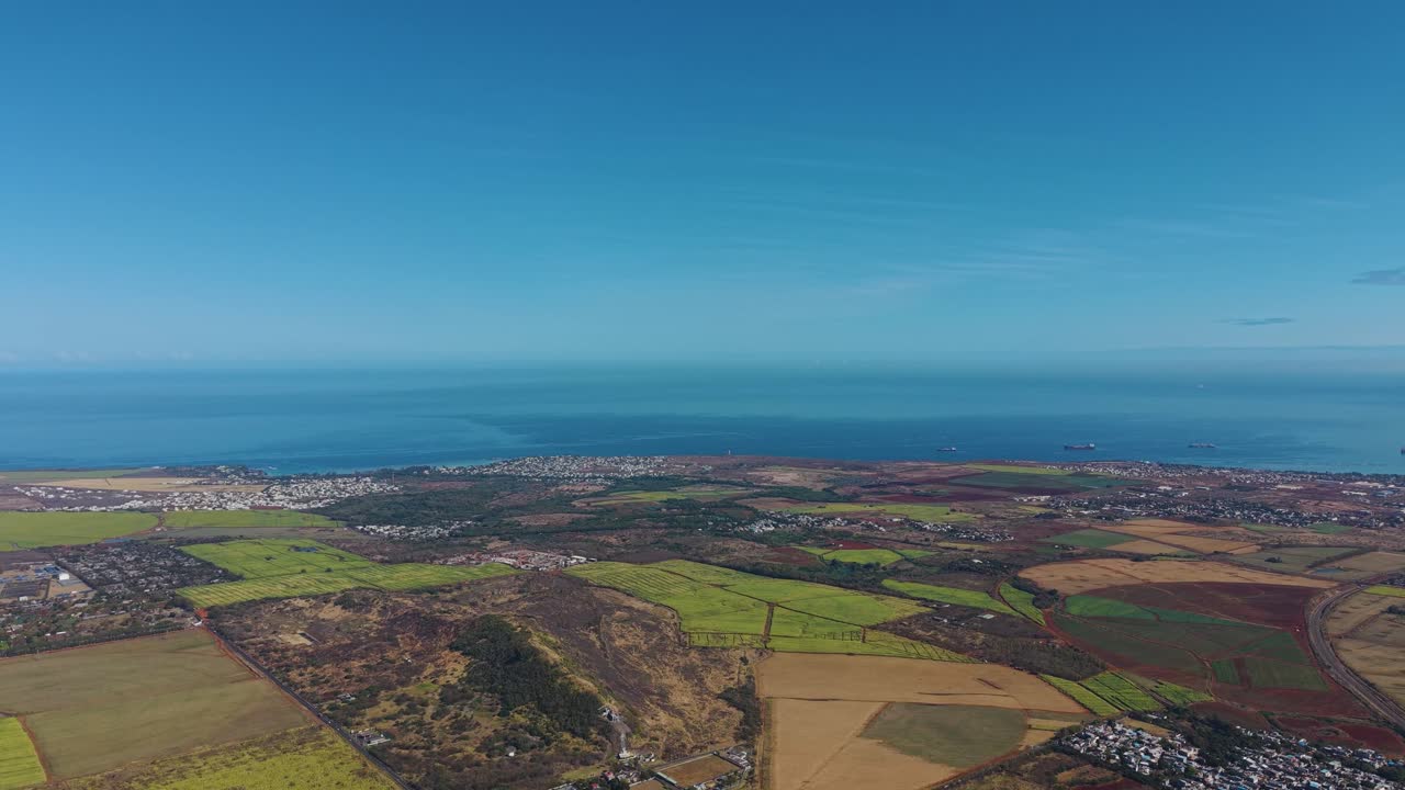 Aerial view over Mauritius, capturing the vibrant contrast of a seaside town, lush fields, and the deep blue Indian Ocean. Perfect for travel, nature, and documentary projects