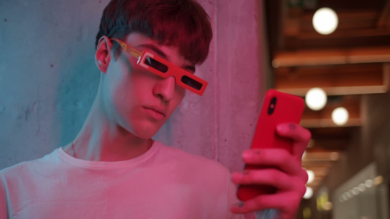 A young man uses his phone in a neon-lit setting