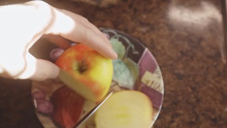 female hands with a kitchen knife slicing apple on the countertop at home