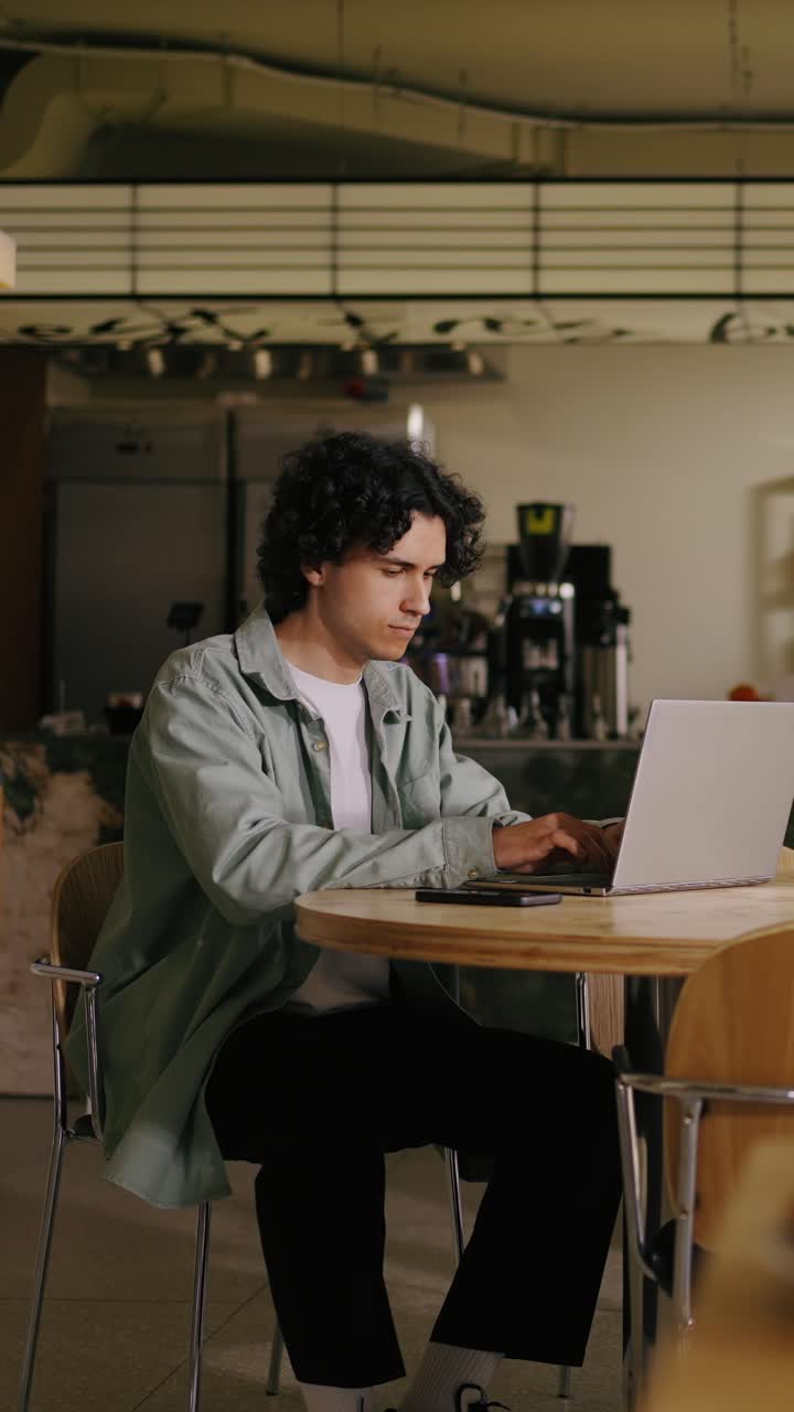 Giovane uomo con i capelli ricci che digita al laptop in un caffè