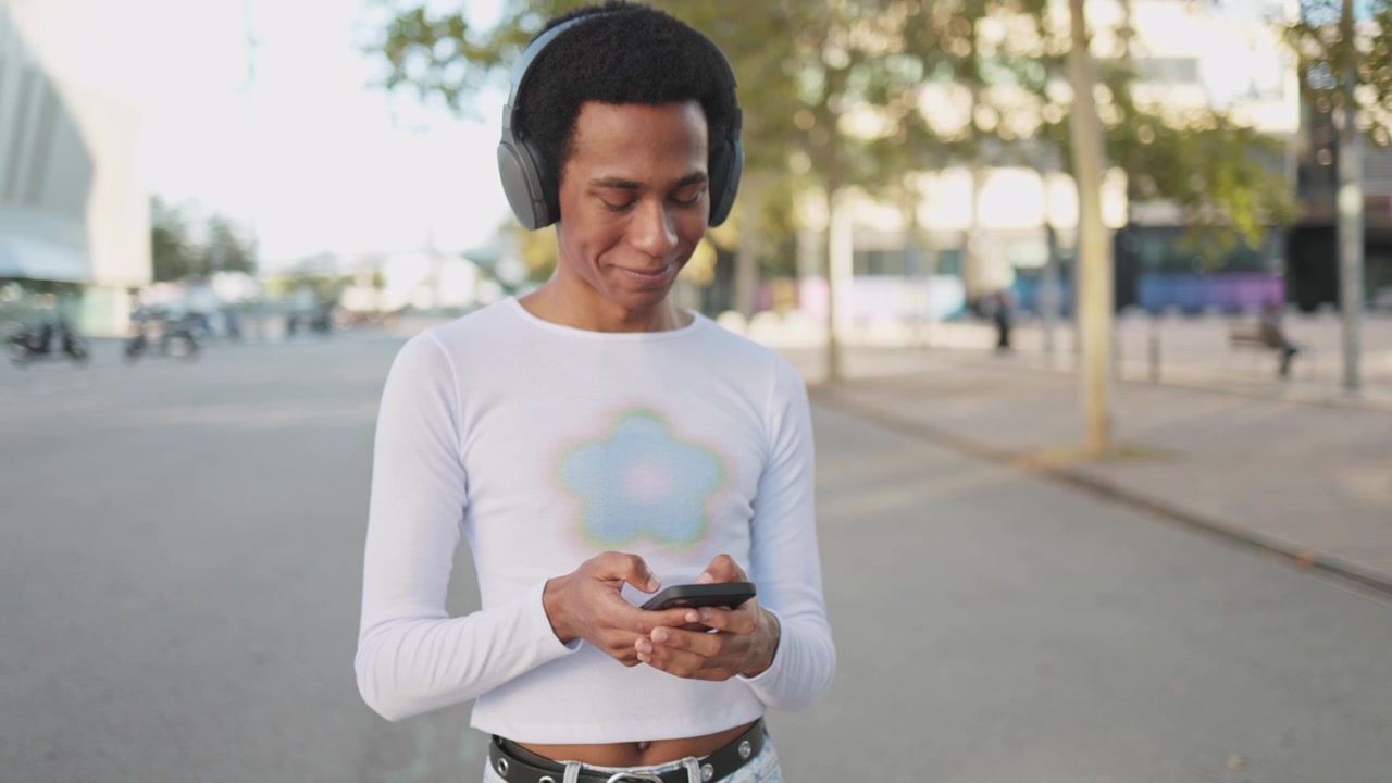 Giovane uomo felice con le cuffie che usa lo smartphone all'aperto