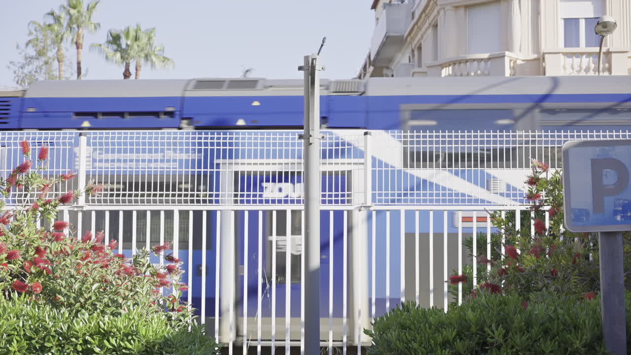 Cannes, Frankrig – 1. maj 2025: Hvidt og blåt tog, der passerer gennem byen bag et hvidt hegn