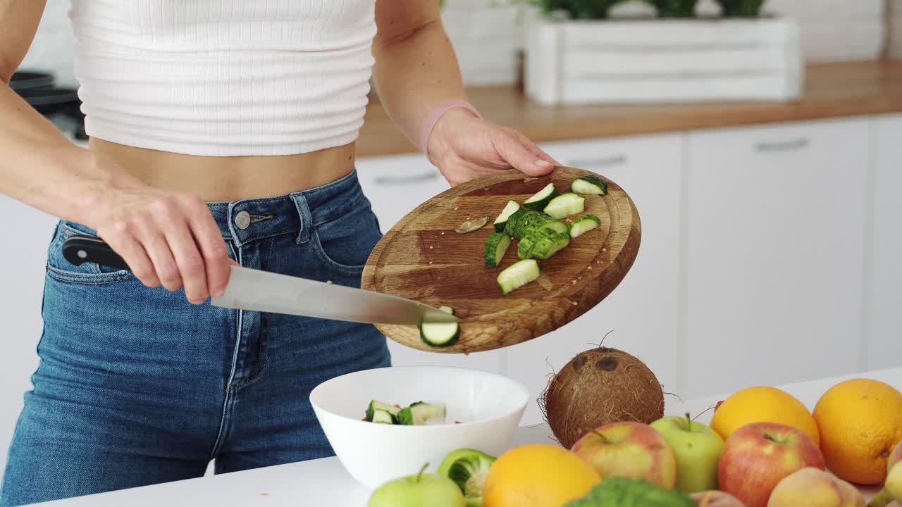 Cutting a green cucumber for salad with a knife on a wooden board. Vegetarian food preparation