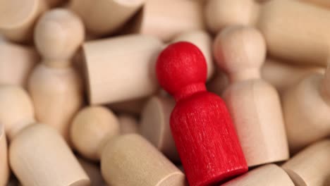 a single red wooden figure stands out among a group of many beige figures, symbolizing individuality or distinction