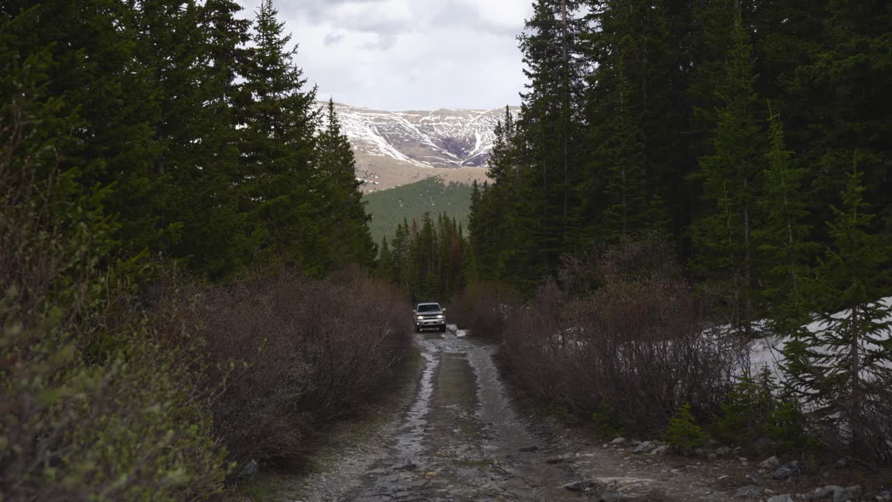Veicolo fuoristrada percorre una strada di montagna bagnata attraverso una foresta innevata primaverile
