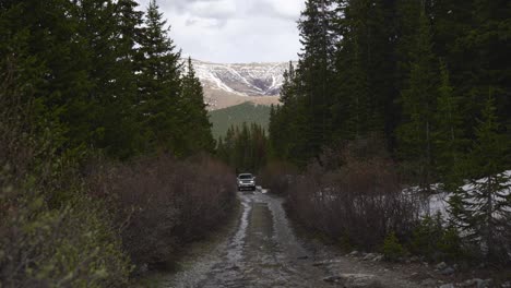 Offroad-vehicle-drives-wet-mountain-road-through-spring-snow-forest