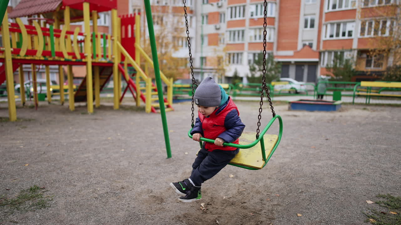 Cute toddler boy sitting on the swing backwards. Baby on the playground in autumn.