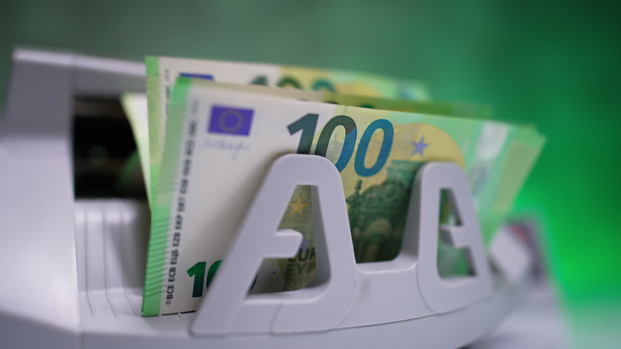 Starting a cash counting machine. Blades of device rotate and new one hundred euro banknotes appear. Close up. Blurred backdrop.