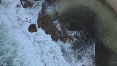Top-view-moving-up-of-sea-foam-crashing-rocks-in-Australian-beach-coastline