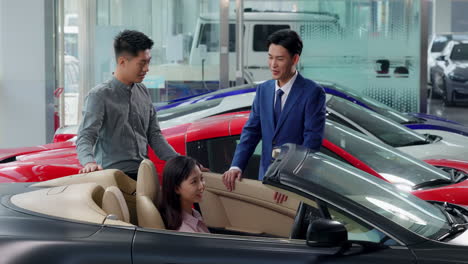 couple with attractive auto dealer in a suit presenting new car model to his client